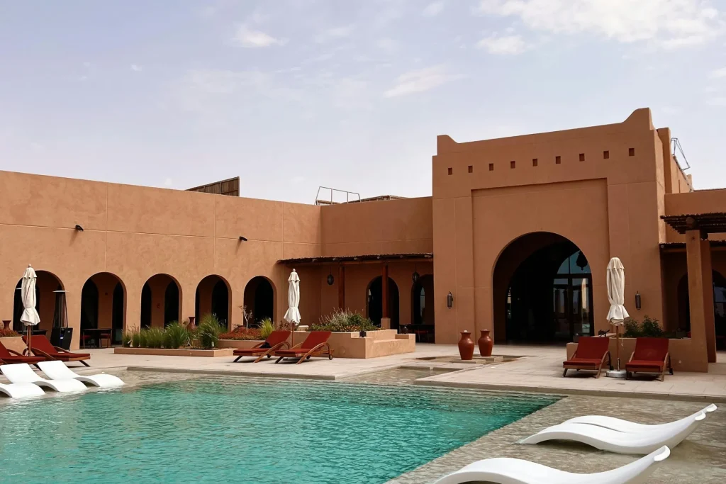 Piscine de villa de luxe à Marrakech, Maroc, avec chaises longues blanches, arches mauresques et murs en terre cuite.