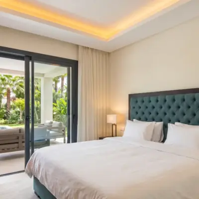 Chambre de luxe avec tête de lit en velours sarcelle, linge blanc et accès terrasse sur jardin tropical