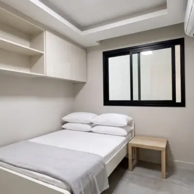 Chambre de personnel compacte avec rangements encastrés, lit simple blanc, table de chevet en chêne et climatisation
