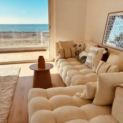 Chambre parentale avec baie toute hauteur ouvrant sur une vue mer panoramique, fauteuil en bouclé crème et tapis en laine