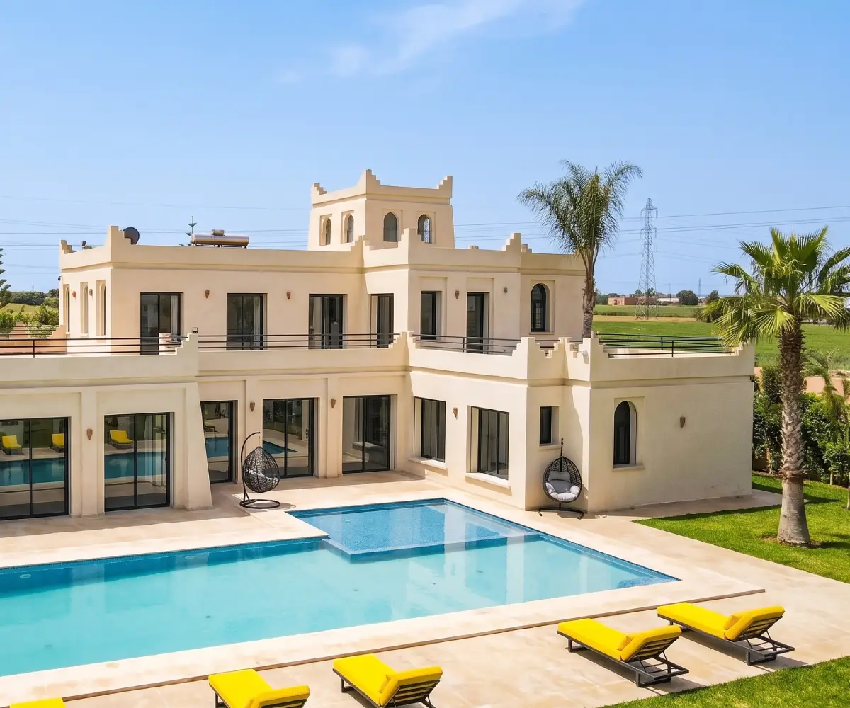 Villa de style marocain près de Casablanca avec tour crénelée, fenêtres cintrées et transats jaunes au bord de la piscine