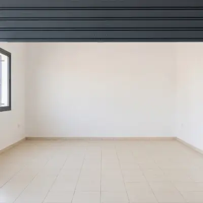 Intérieur d'un garage à louer à Agadir, avec rideau métallique relevé, fenêtre à barreaux et sol carrelé clair