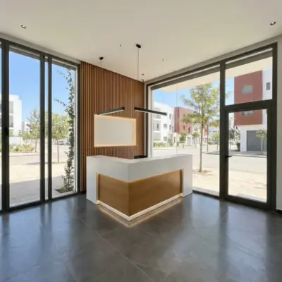Espace d'accueil d'un local commercial à Meknès, banque en L blanc et chêne, mur à tasseaux bois et baies vitrées