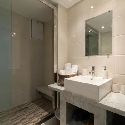 Salle de bains avec douche à l’italienne, meuble vasque en marbre de Carrare, vasque à poser et serviettes roulées