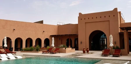 Piscine de villa de luxe à Marrakech, Maroc, avec chaises longues blanches, arches mauresques et murs en terre cuite.