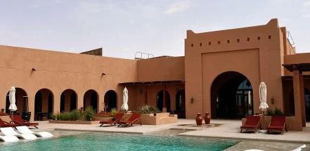 Piscine de villa de luxe à Marrakech, Maroc, avec chaises longues blanches, arches mauresques et murs en terre cuite.